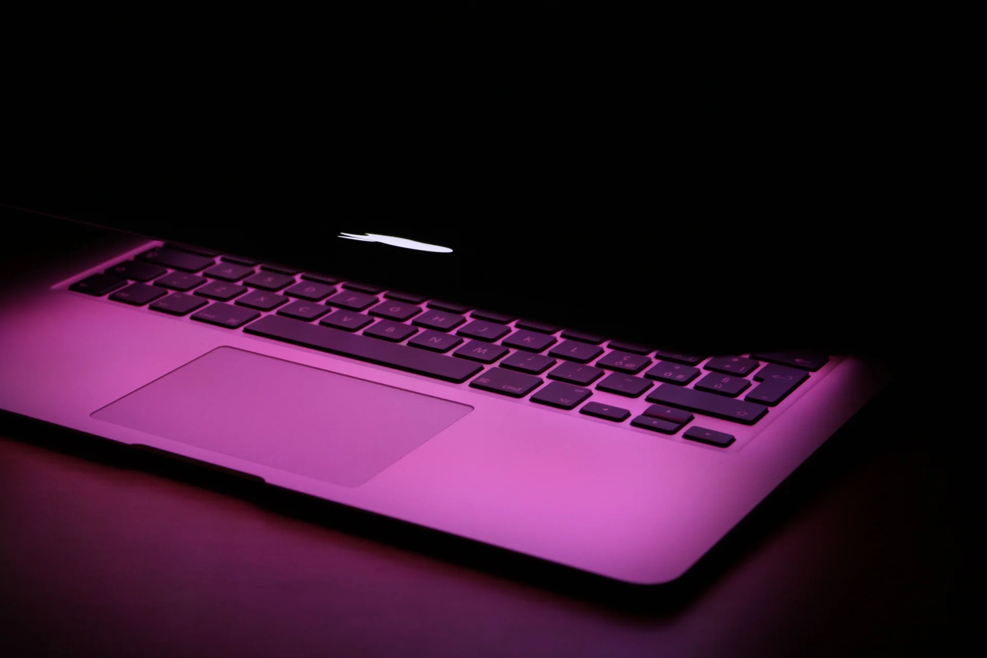 Stylowy laptop częściowo zamknięty, oświetlony różowym światłem, podkreślającym jego nowoczesny design.