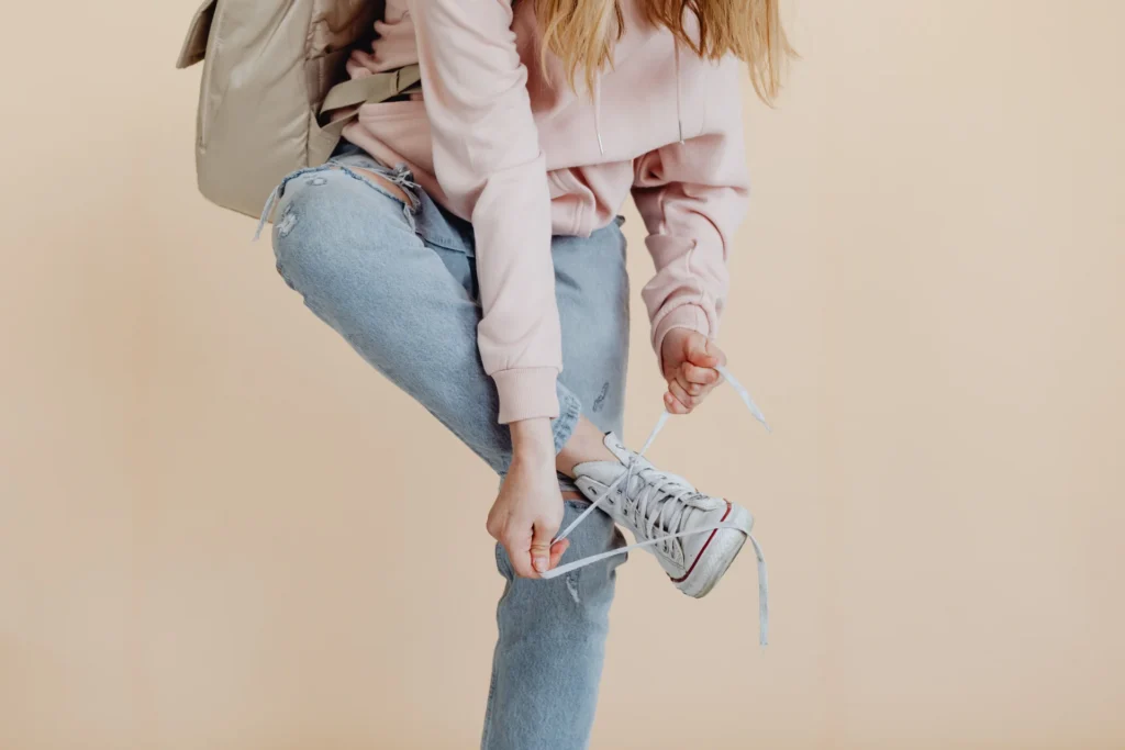 Kobieta w dżinsach i różowej bluzce wiąże sznurowadła białych sneakersów, modny wygląd.