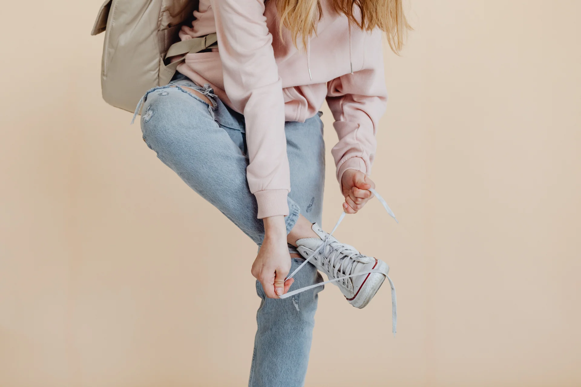 Kobieta w dżinsach i różowej bluzce wiąże sznurowadła białych sneakersów, modny wygląd.